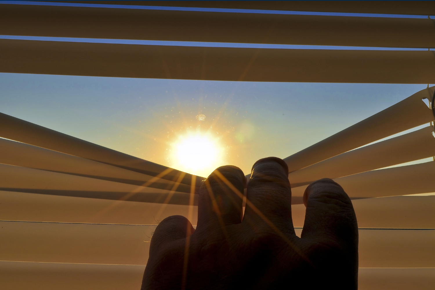 mano che abbassa le veneziane di una tenda da cui si intravede il sole