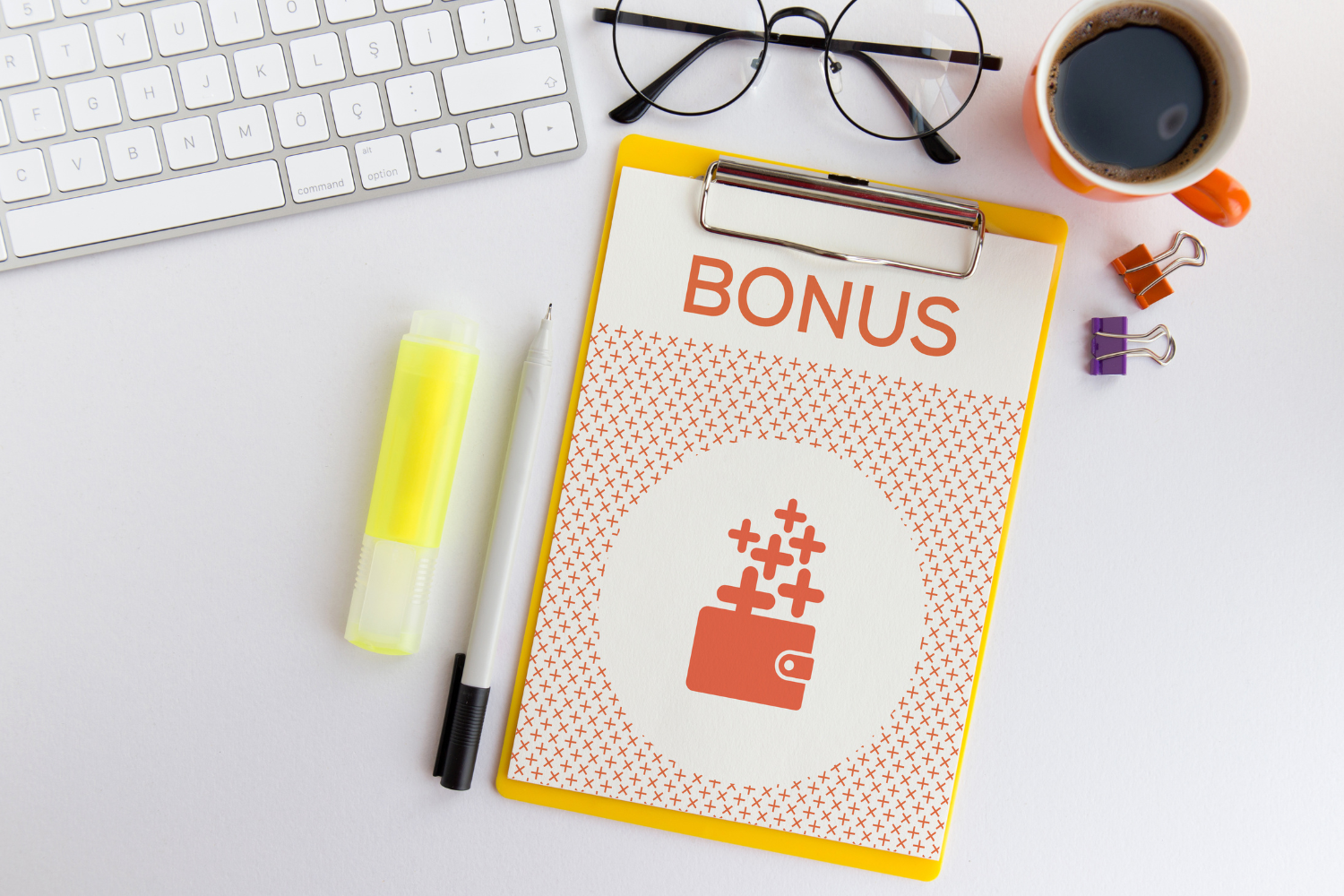 scrivania di ufficio con tastiera, penna, evidenziatore, occhiali, caffè e foglio su cui si legge la scritta "bonus"