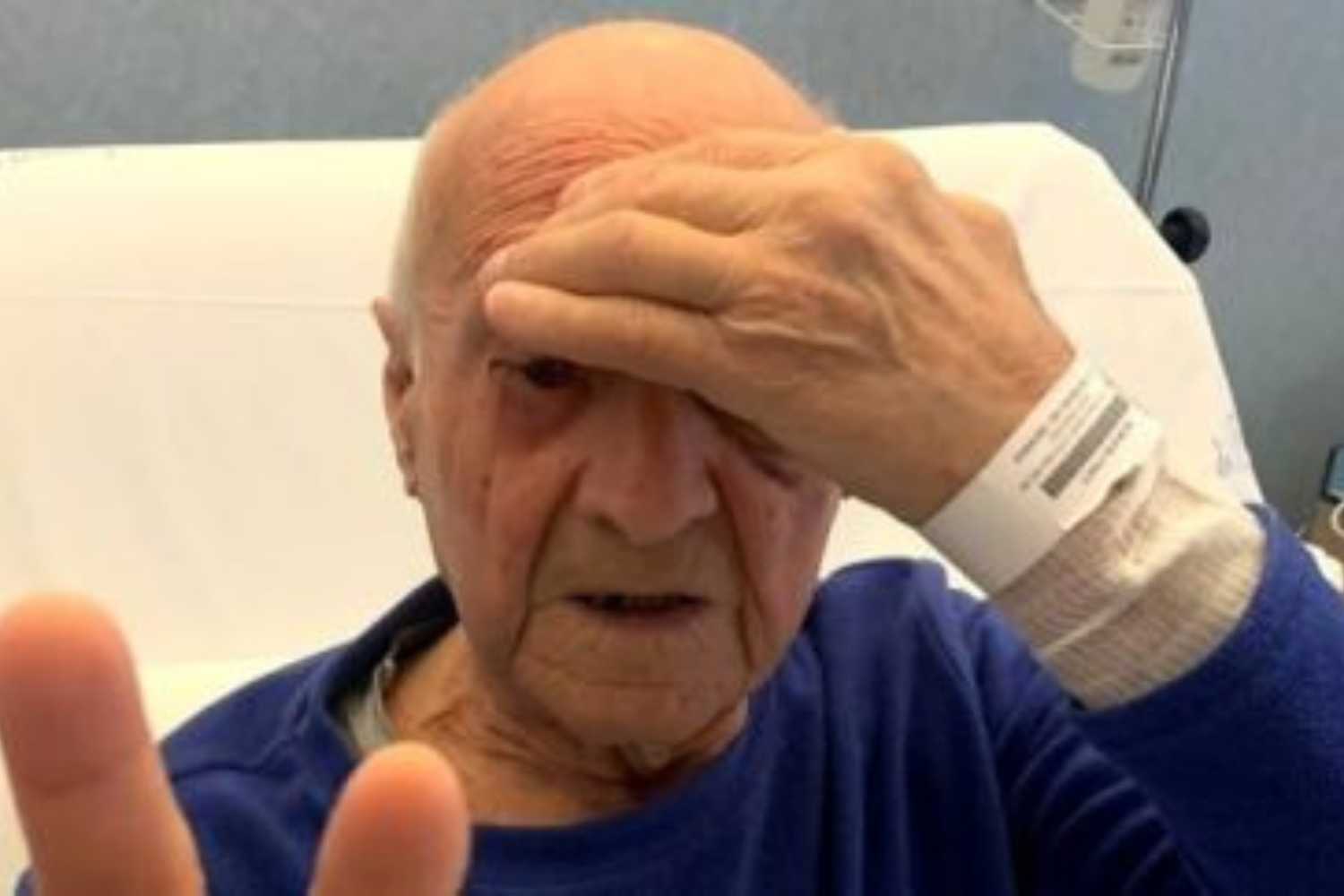anziano signore seduto in un letto di ospedale con una mano sulla fronte