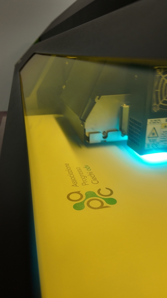Testina di una stampante a rullo Roland in funzione su un pannello con il logo APC, ripresa da vicino durante la stampa.