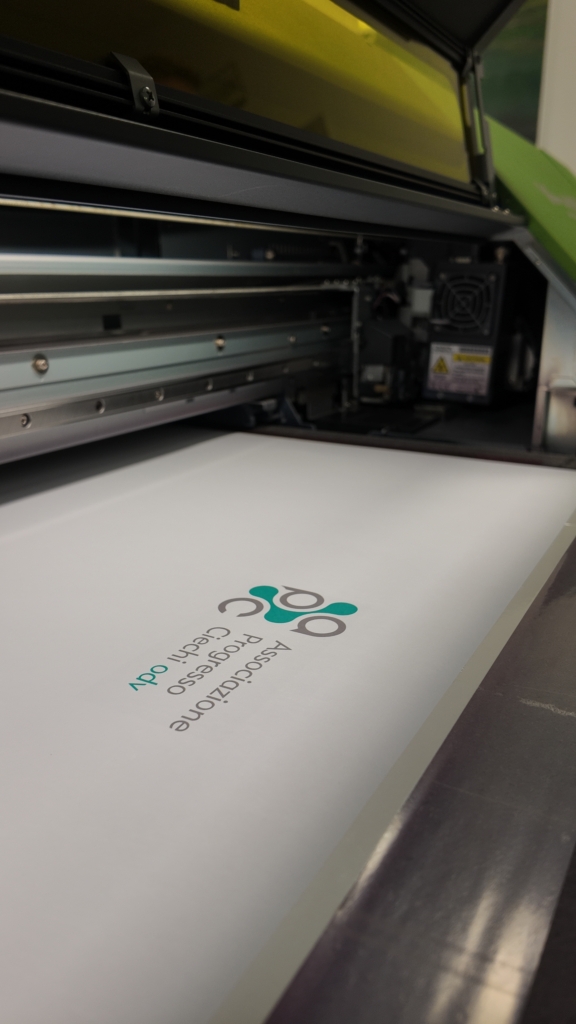 Foglio bianco con il logo APC appena stampato, in uscita dalla macchina da stampa.
